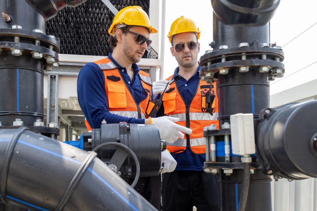 Two industrial workers in safety vests discussing equipment operations to prevent maintenance scheduling inefficiencies.