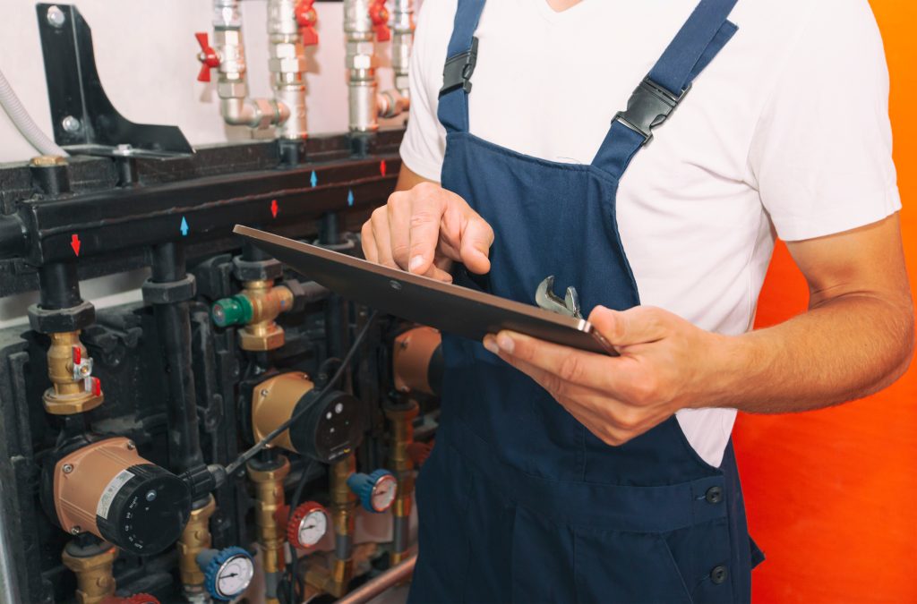 A technician using a tablet to inspect industrial pumps and valves, addressing critical work order management failures.