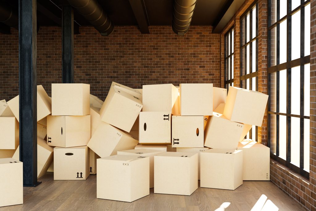 A large pile of disorganized cardboard boxes stacked near a window, illustrating e-commerce product return accumulation in a storage facility.