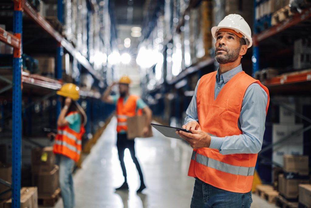 A warehouse manager using a digital tablet on the fulfillment floor to monitor multi-location inventory control and real-time stock transfers.